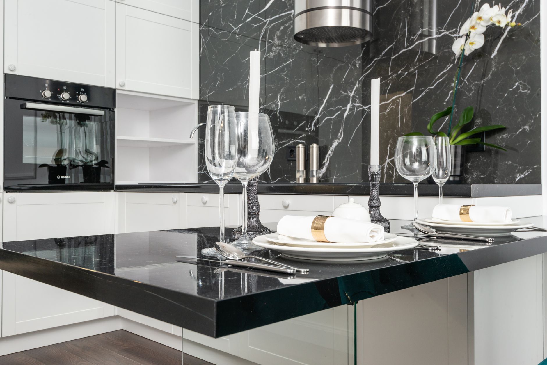 Empty goblets with candlesticks served on black table near plates with rolled napkins in creative kitchen with white